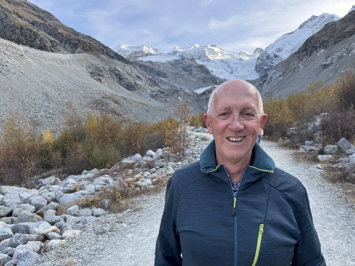 Larry Luke smiling on a gravel trail with a snowy glacier-capped mountain behind him