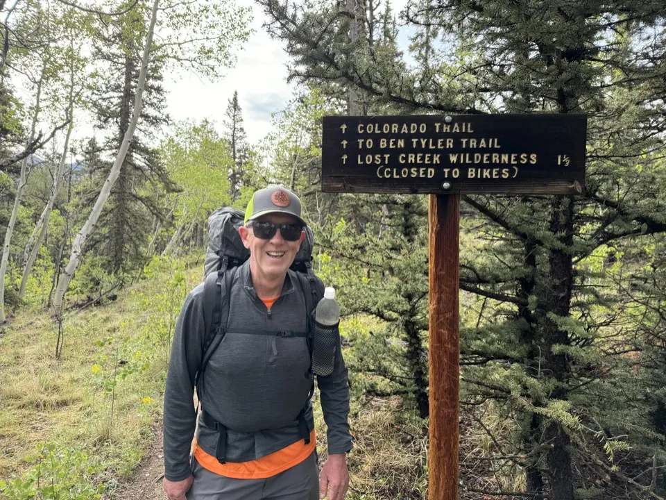Larry Luke with a backpack beside a Colorado Trail sign