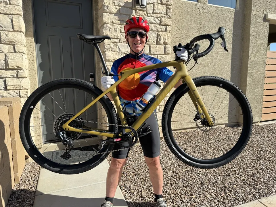 Larry Luke in a cycling kit holding up his gravel bike