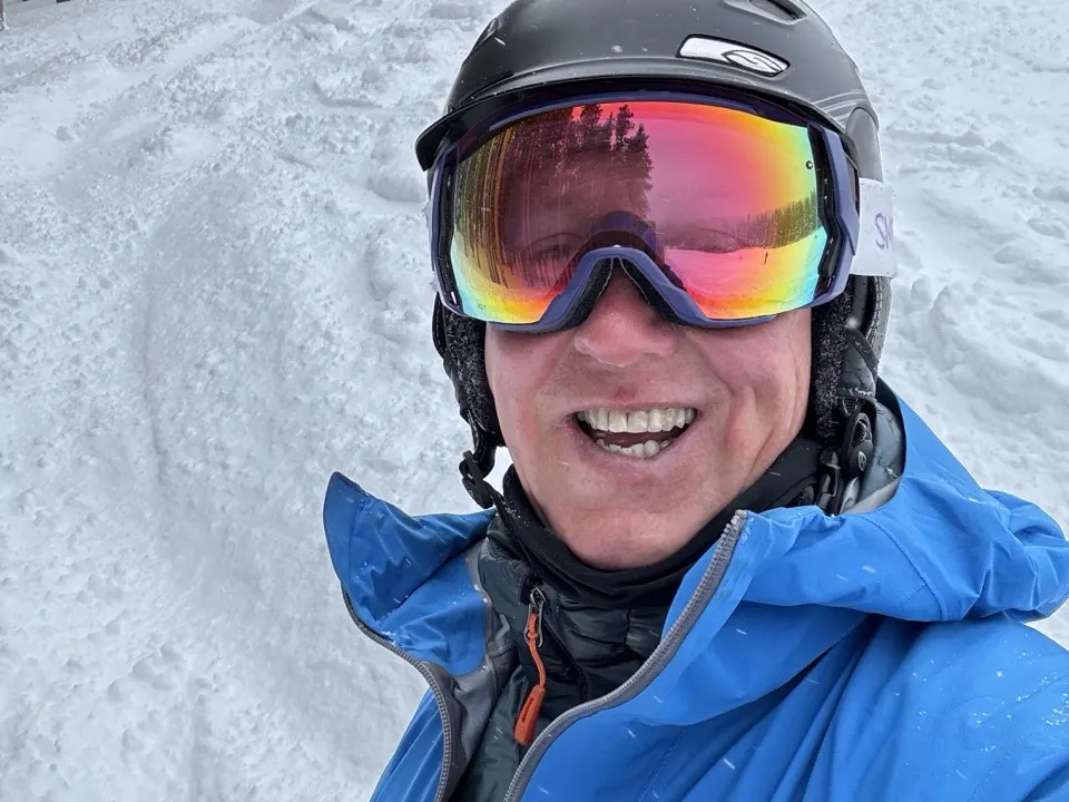 Larry Luke smiling in a helmet and goggles on a snowy ski run