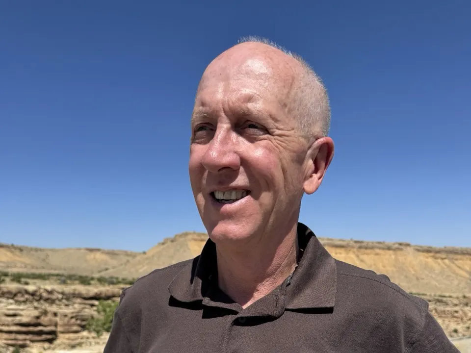 Larry Luke smiling in front of sandstone bluffs under a deep blue sky